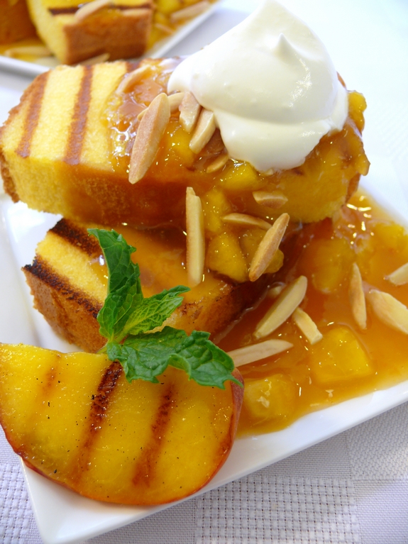 Grilled pound cake, warm peach coulis with a chantilly cream sauce on a white plate with mint garnish.