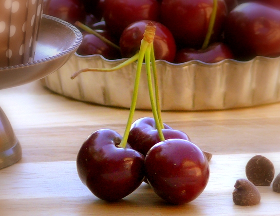 Fresh cherries in a tin and some with stems and a few chocolate chips.