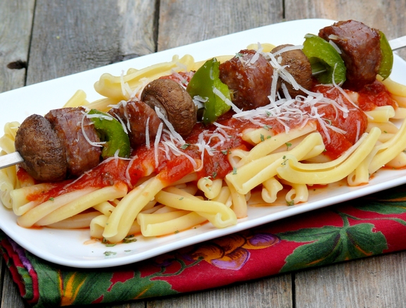 These deliciously grilled Sausage Kabobs served with Pasta are a fun and easy dinner to prepare. They are especially loved by kids. Sausage kabob sitting on top of pasta with marinara.