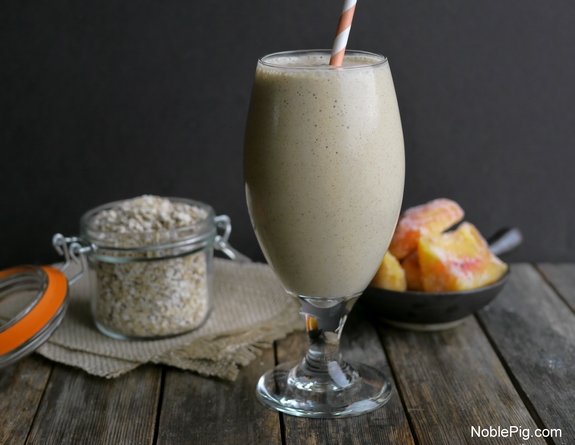 Peach Cinnamon Oatmeal Smoothie in a tall glass, oatmeal jar and peach behind it.