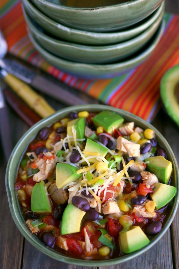 This Mexican Chicken Soup with Avocado will have a delicious and satisfying dinner on the table in 15-minutes. Some nights we need all the help we can get. 15 Minute Mexican Chicken Soup in a bowl with bowls in the background.