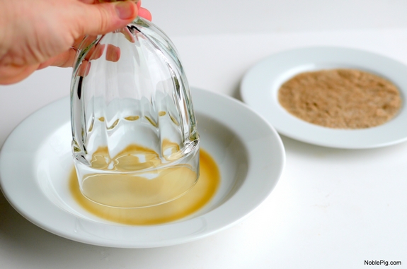 Glass edge being dipped in beer with plate of cinnamon in the background.
