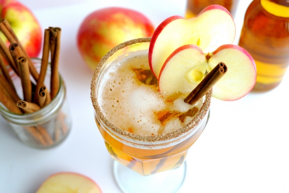 Overhead shot of beer-cider slam with apple slices and cinnamon stick. Jar of cinnamon sticks, apples and bottles of cider.