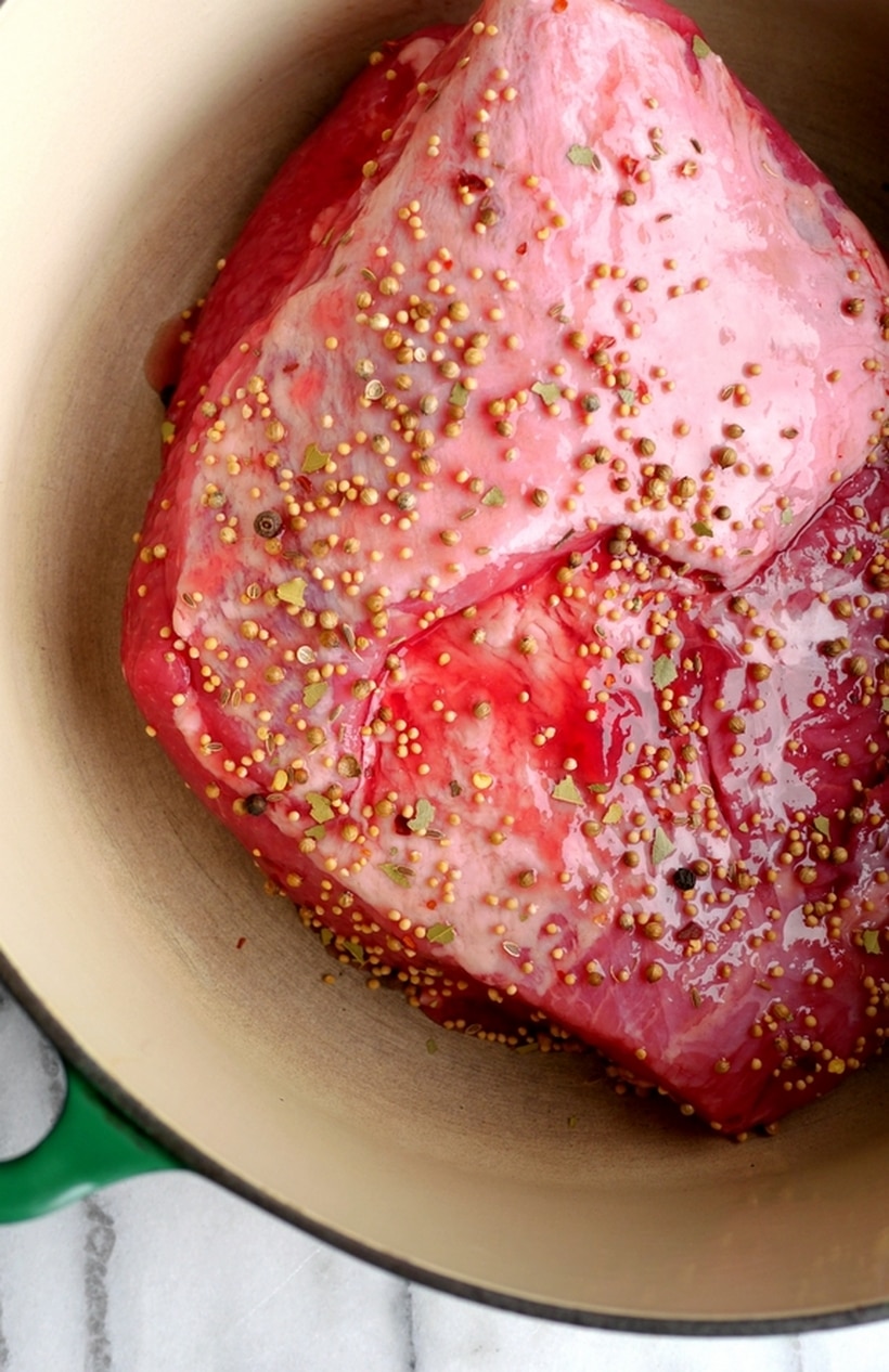 Whiskey-Glazed Corned Beef before cooking Corned beef simmering in a Dutch oven with the spice packet floating on top, surrounded by seasoned broth.