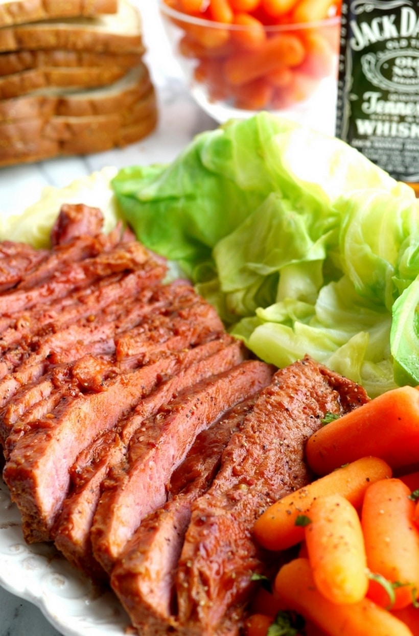 Whiskey-Glazed Corned Beef on a platter Sliced whiskey-glazed corned beef arranged on a platter with roasted carrots and cabbage, ready to serve.