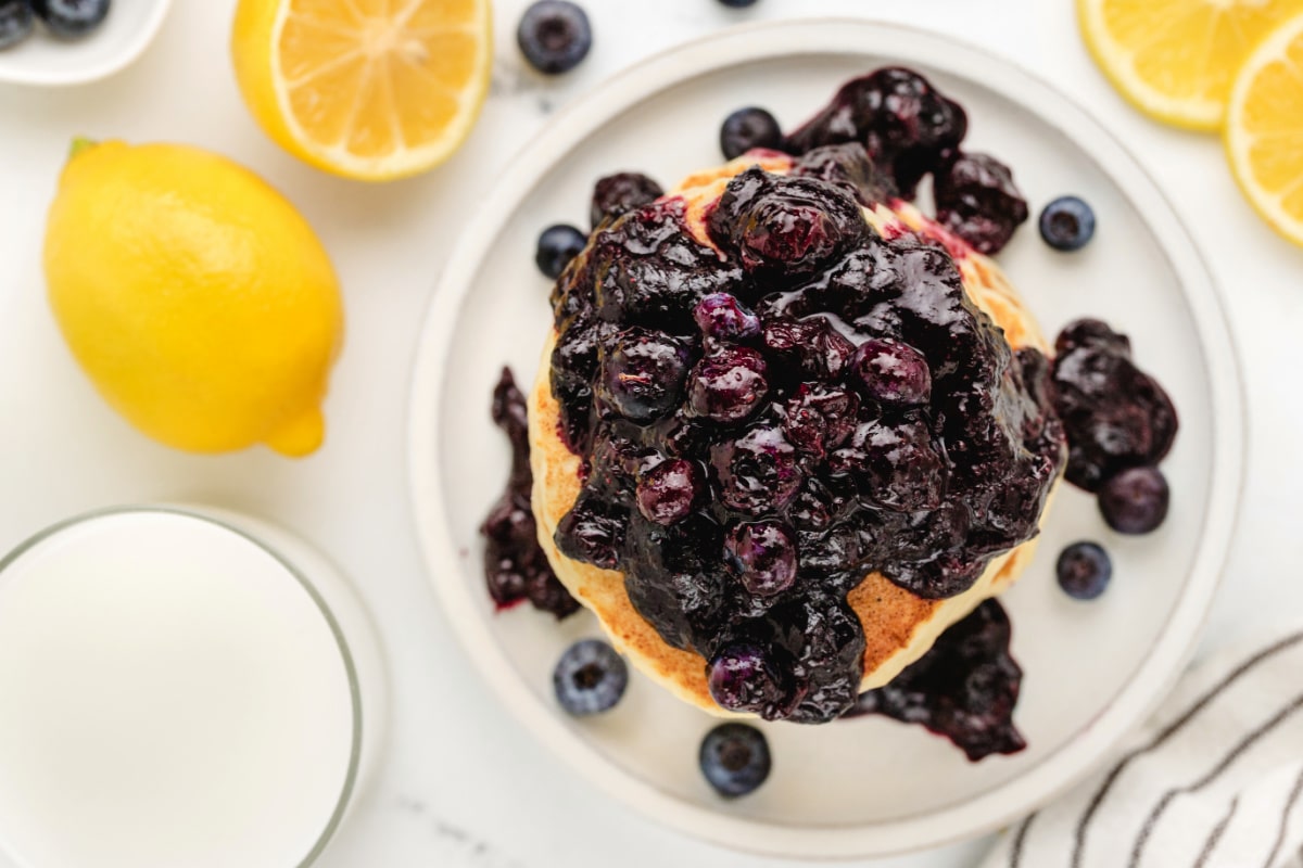 Overhead shot of a stack of fluffy lemon ricotta pancakes topped with glossy blueberry sauce, highlighting the deep color contrast.