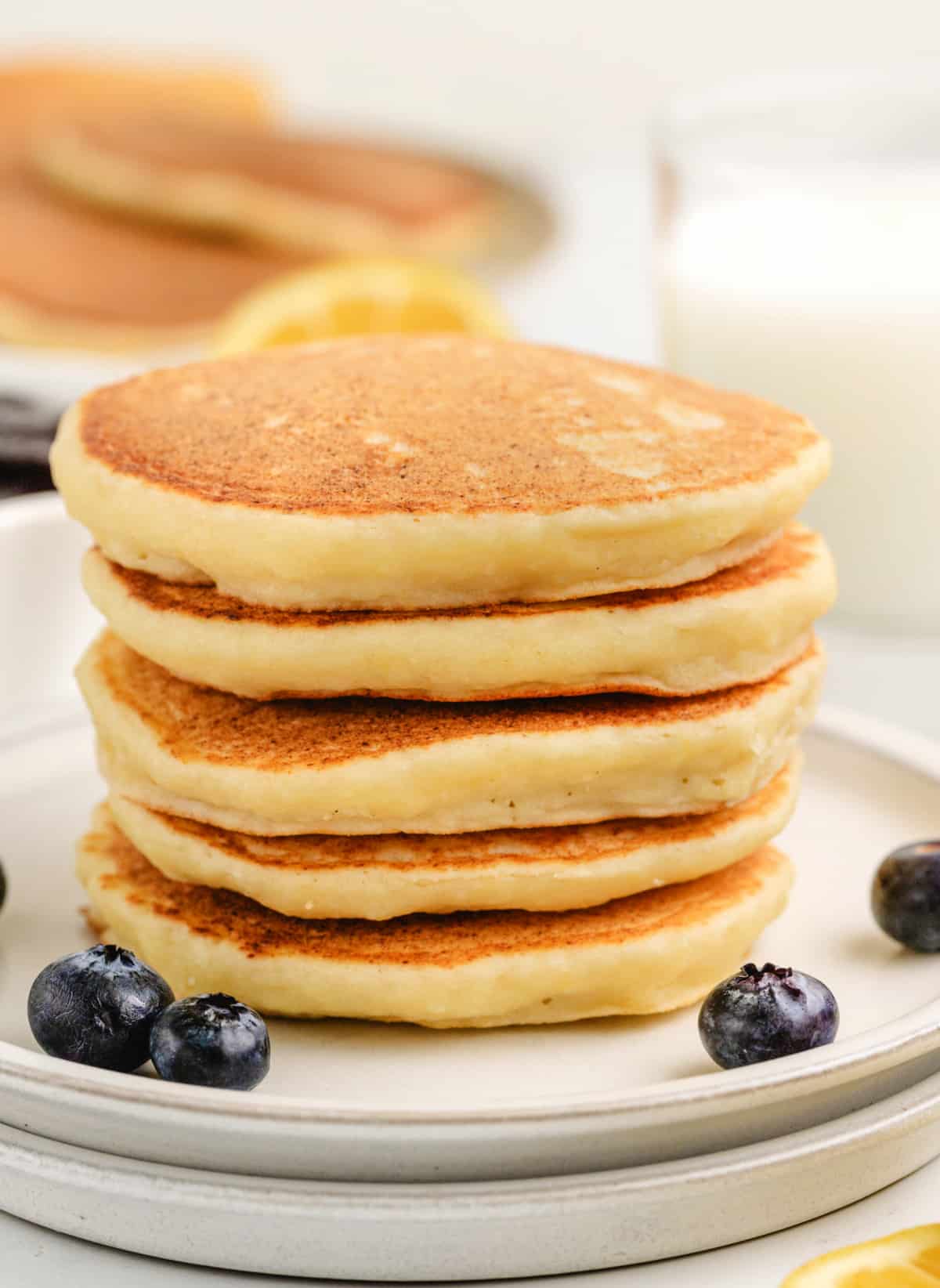 A stack of plain lemon ricotta pancakes, golden brown and fluffy, served on a plate before adding the blueberry sauce.