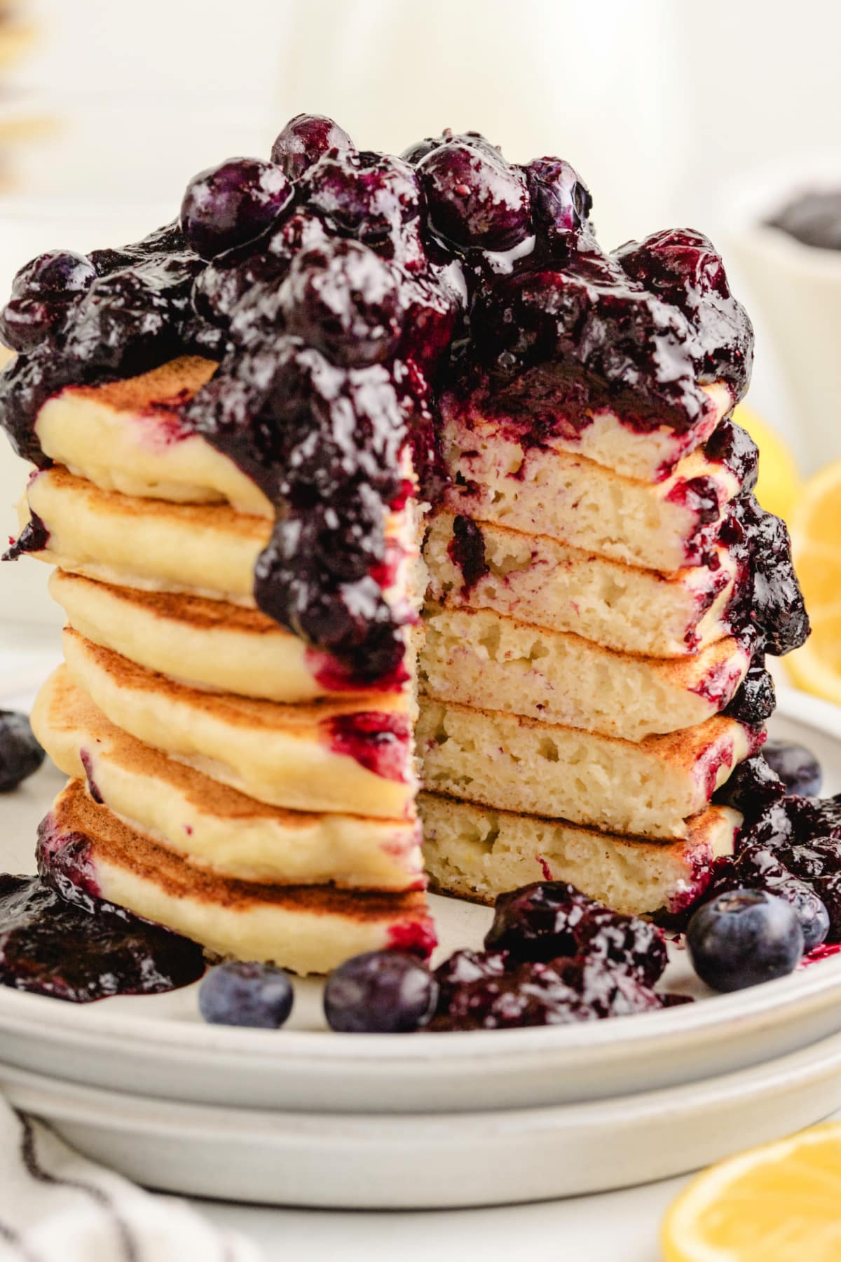 A stack of lemon ricotta pancakes drizzled with blueberry sauce, with a full bite removed, showing the soft, fluffy interior.