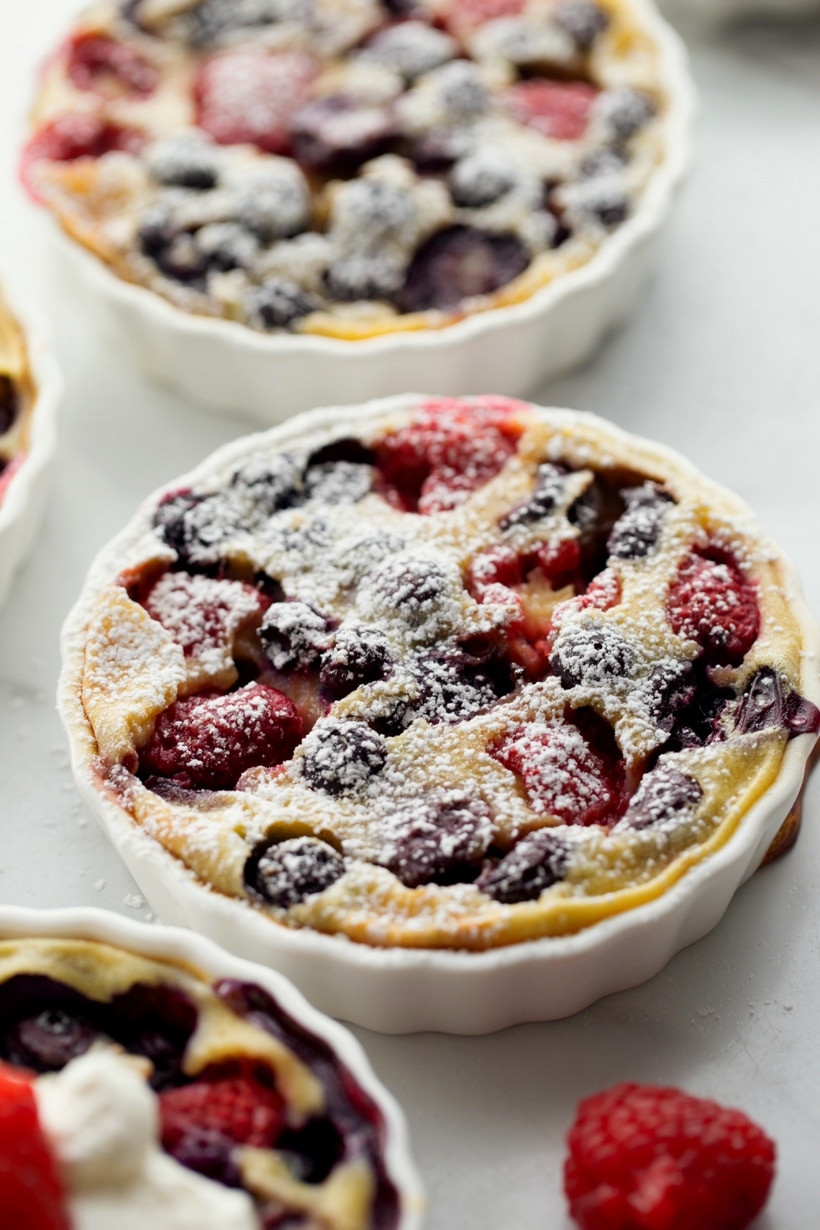 Enjoy the taste of summer with this mixed berry and cherry clafoutis. This dessert features ripe cherries and berries baked into a creamy custard. clafoutis with powdered sugar