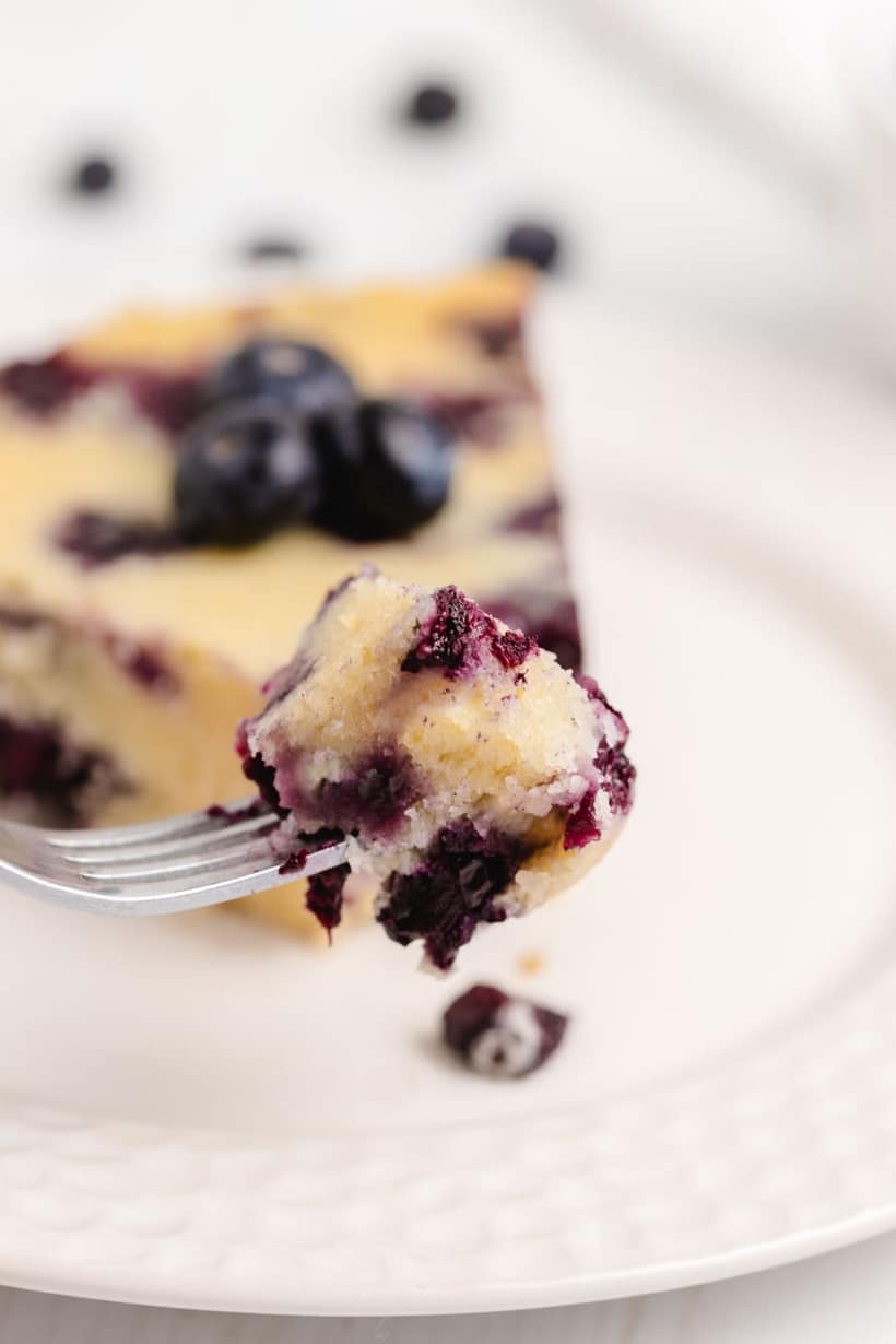 Single bite of blueberry coffee cake on a fork, showing crumb and berries