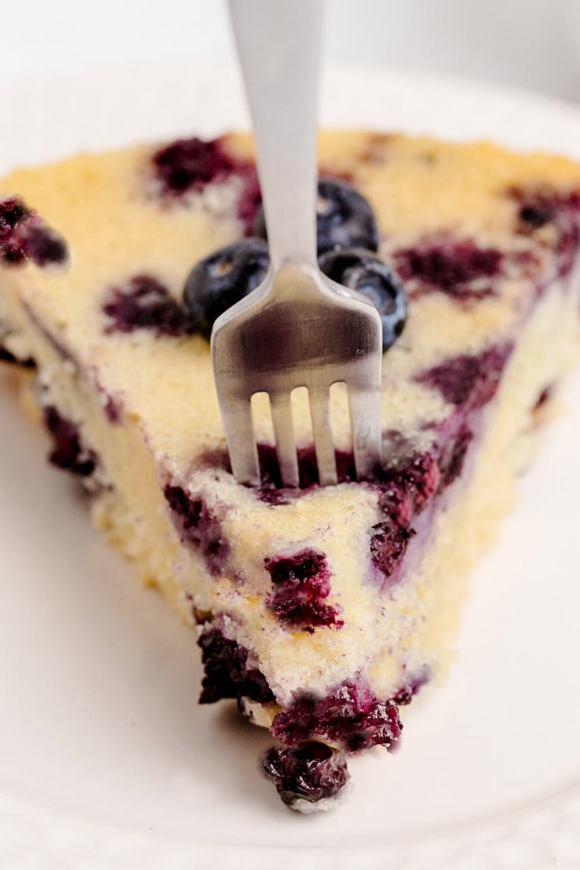 Fork digging into a slice of blueberry coffee cake, showing soft inside and crust