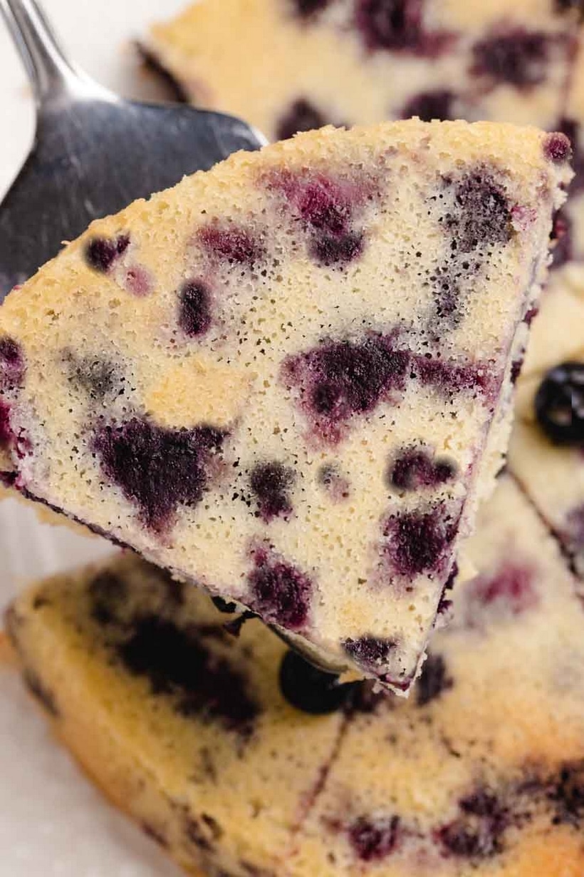 Slice of blueberry coffee cake being lifted out on a spatula, crust visible on the bottom