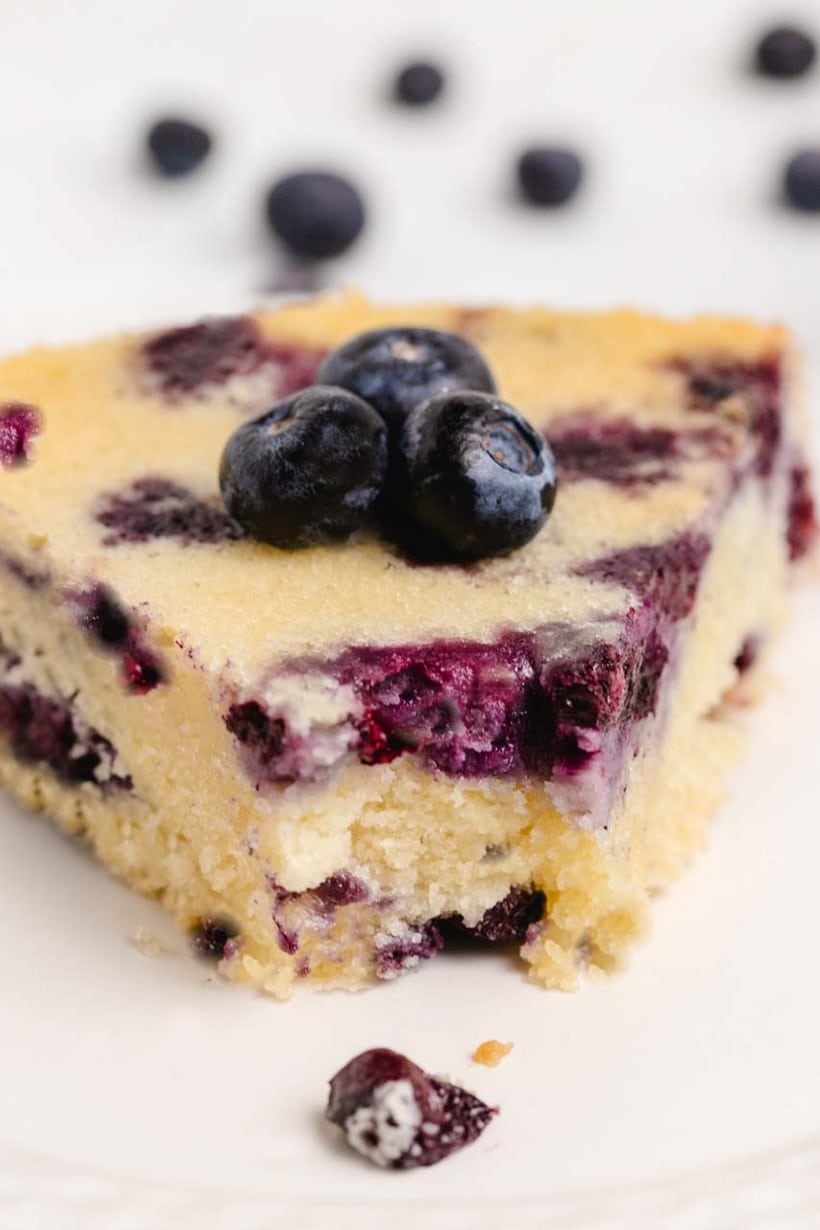 Close-up of a slice of blueberry coffee cake with a bite taken out, showing the crisp sugar crust