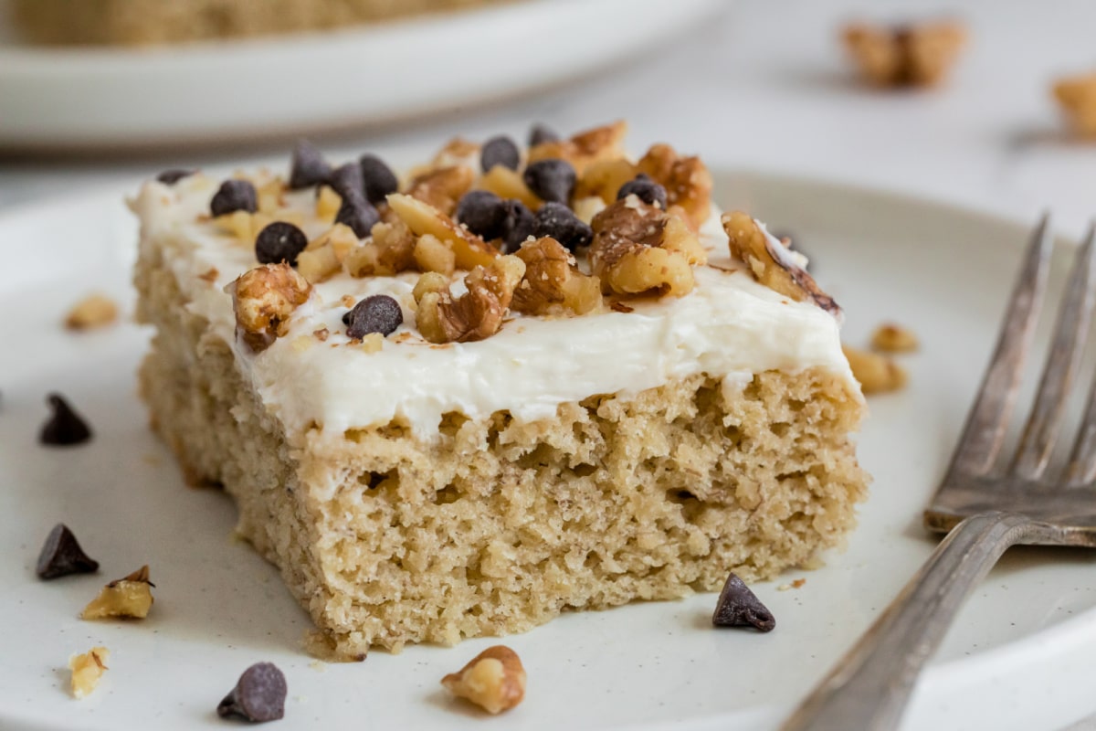 a slice of Banana Sheet Cake with Cream Cheese Sour Cream Frosting A single slice of banana sheet cake with cream cheese sour cream frosting on a white plate.