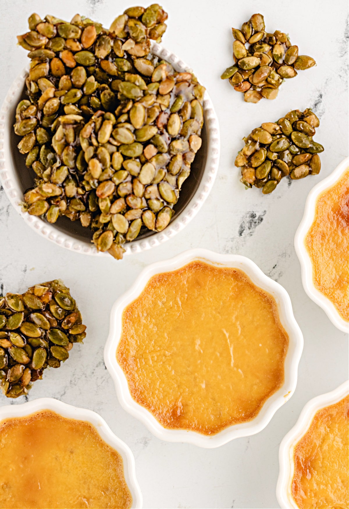pepita brittle with pumpkin chai custard Pepita brittle cooling next to baked pumpkin chai custards, highlighting the crackly caramel contrast to the smooth pots de crème.