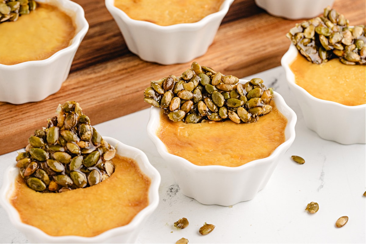 pumpkin chai custards with pepita brittle Pumpkin Chai Pots de Crème by Noble Pig arranged in white ramekins with crisp pepita brittle for a grown-up fall dessert.