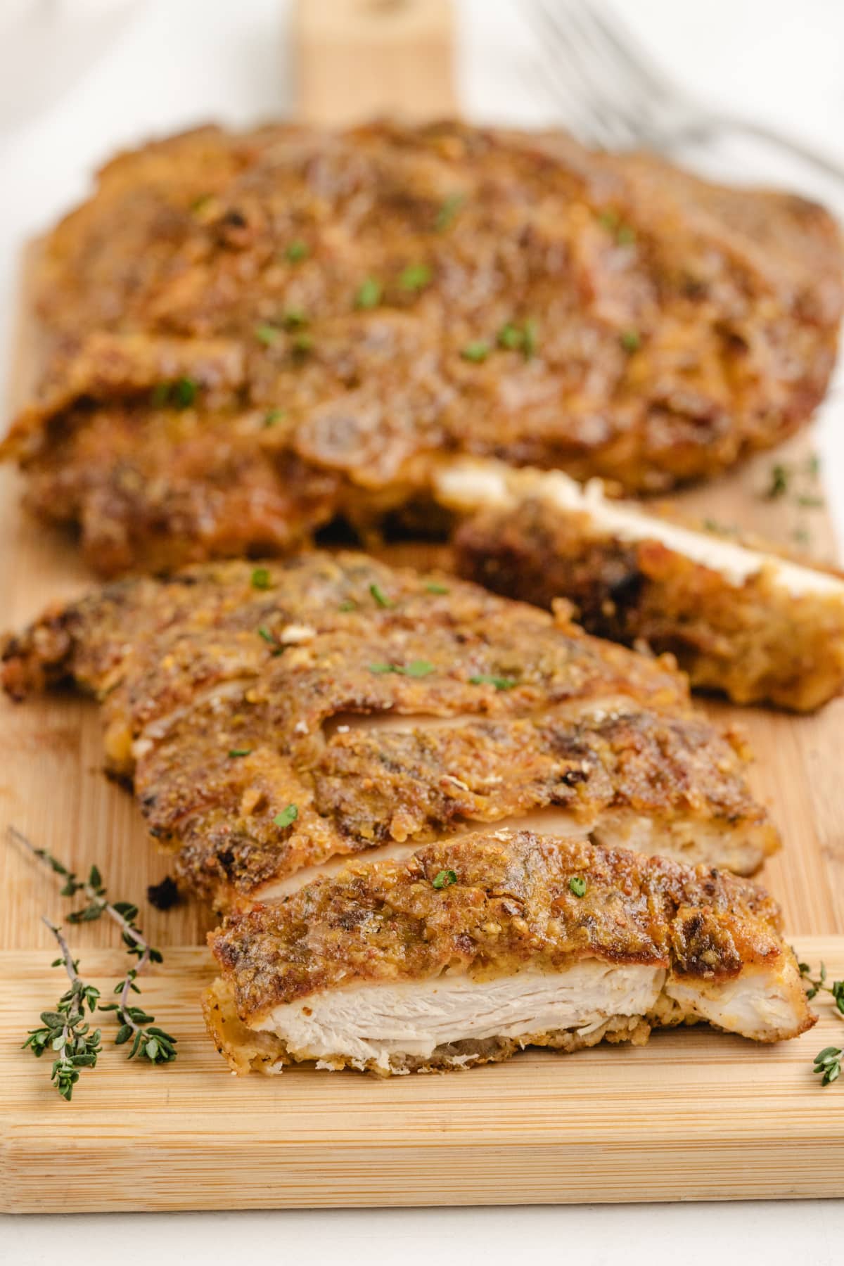 Sliced maple mustard glazed chicken cutlet on a wooden cutting board with fresh thyme