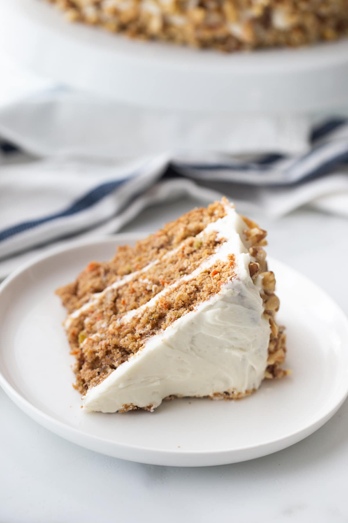 Slice of carrot apple cake on a white plate with the rest of the cake visible in the background.