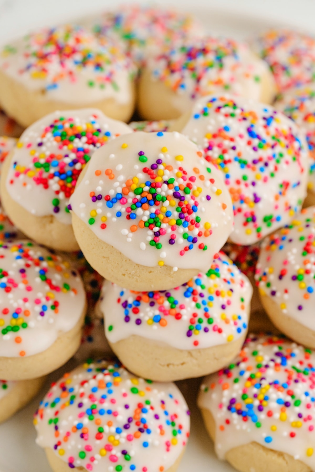 Italian cookies with white glaze and rainbow sprinkles piled on a plate
