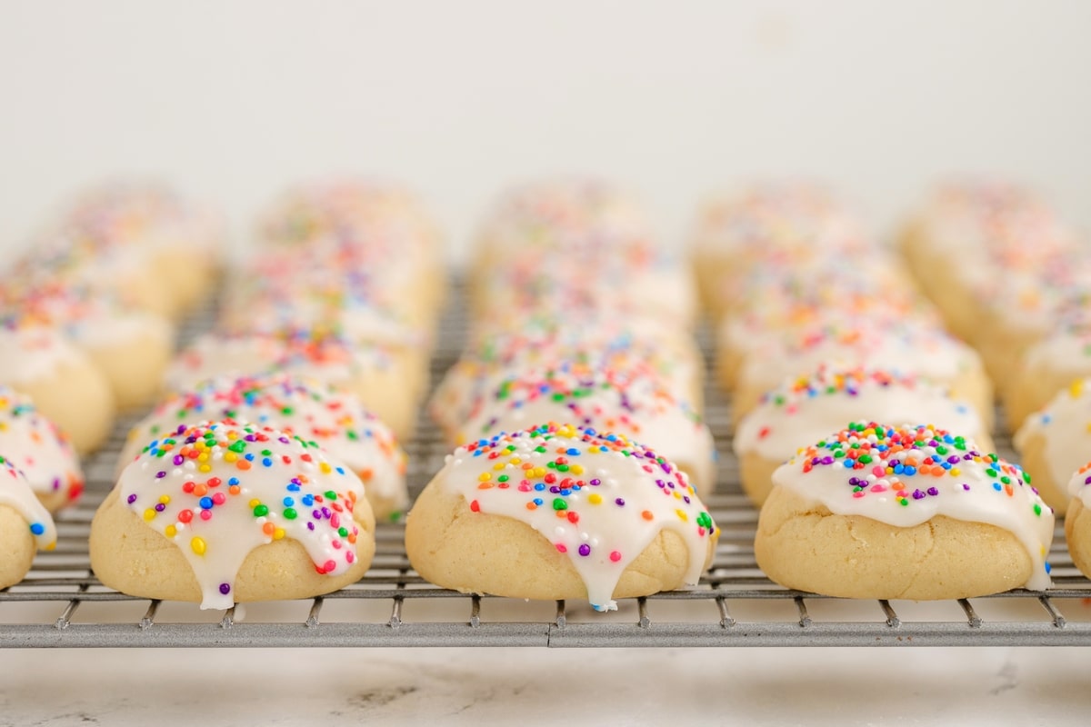 Italian cookies cooling on a rack with white glaze dripping and rainbow sprinkles