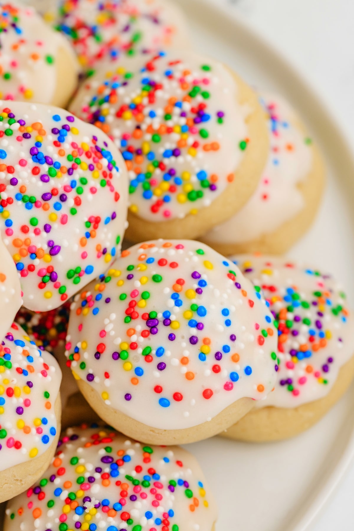 close up of soft Italian cookies with thick white glaze and colorful sprinkles