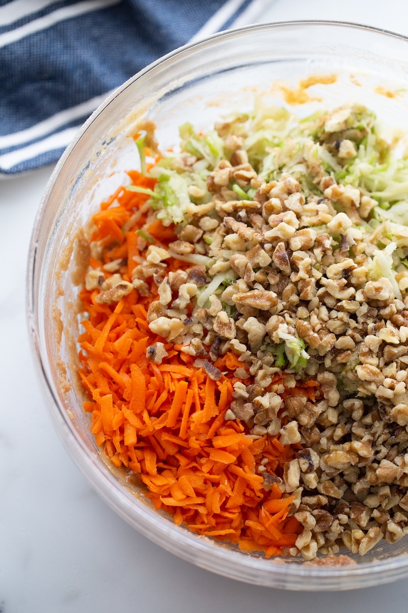 Top view of a mixing bowl filled with shredded carrots, apples, and chopped walnuts. 