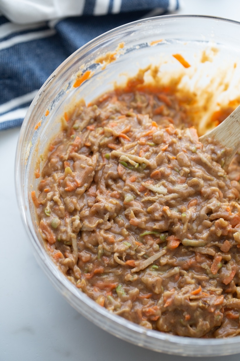 Thick carrot apple cake batter being stirred with a wooden spoon.