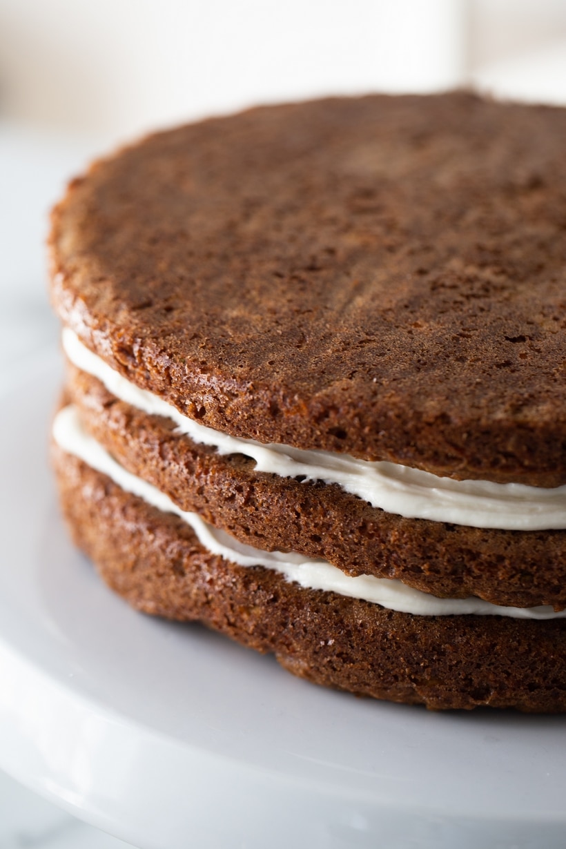 Side view of the cake being frosted, with part of the frosting already smoothed on and part still bare.