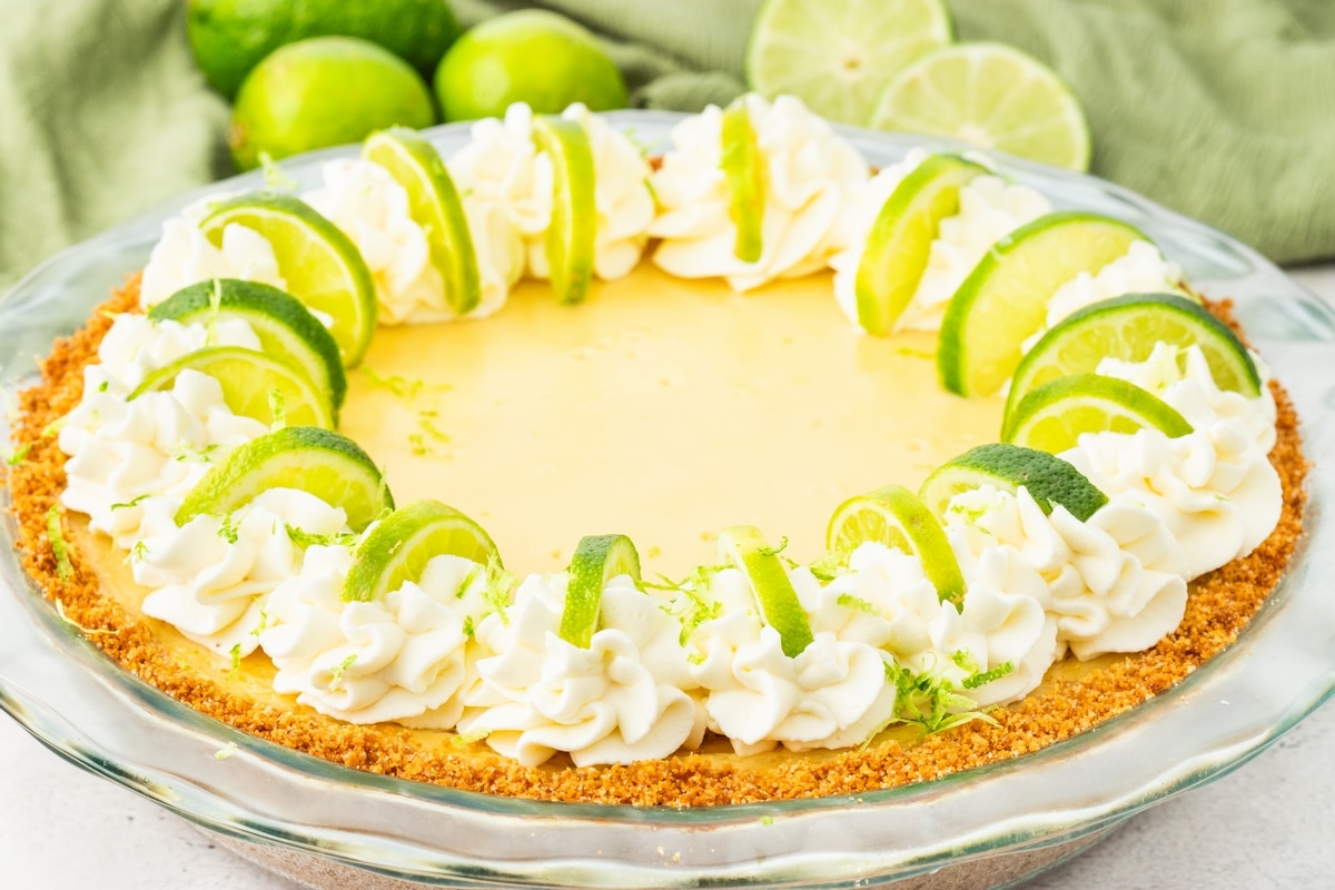 Full key lime pie with whipped cream and lime garnish Side view of a whole key lime pie topped with whipped cream and lime slices