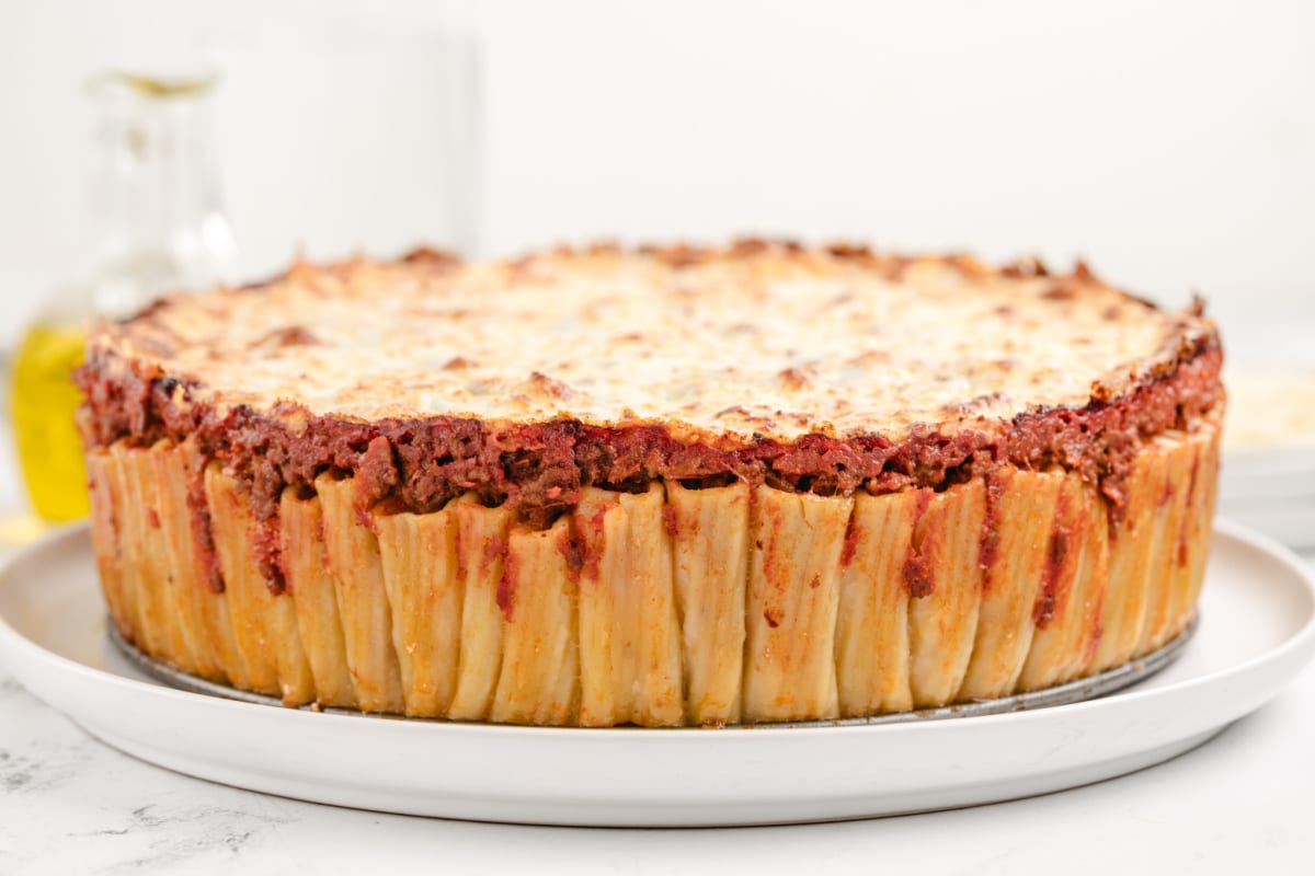 Side view of Pasta Pie A perfectly baked rigatoni pie with crispy, bubbly cheese on top, set on a wooden board, ready to be sliced and served.