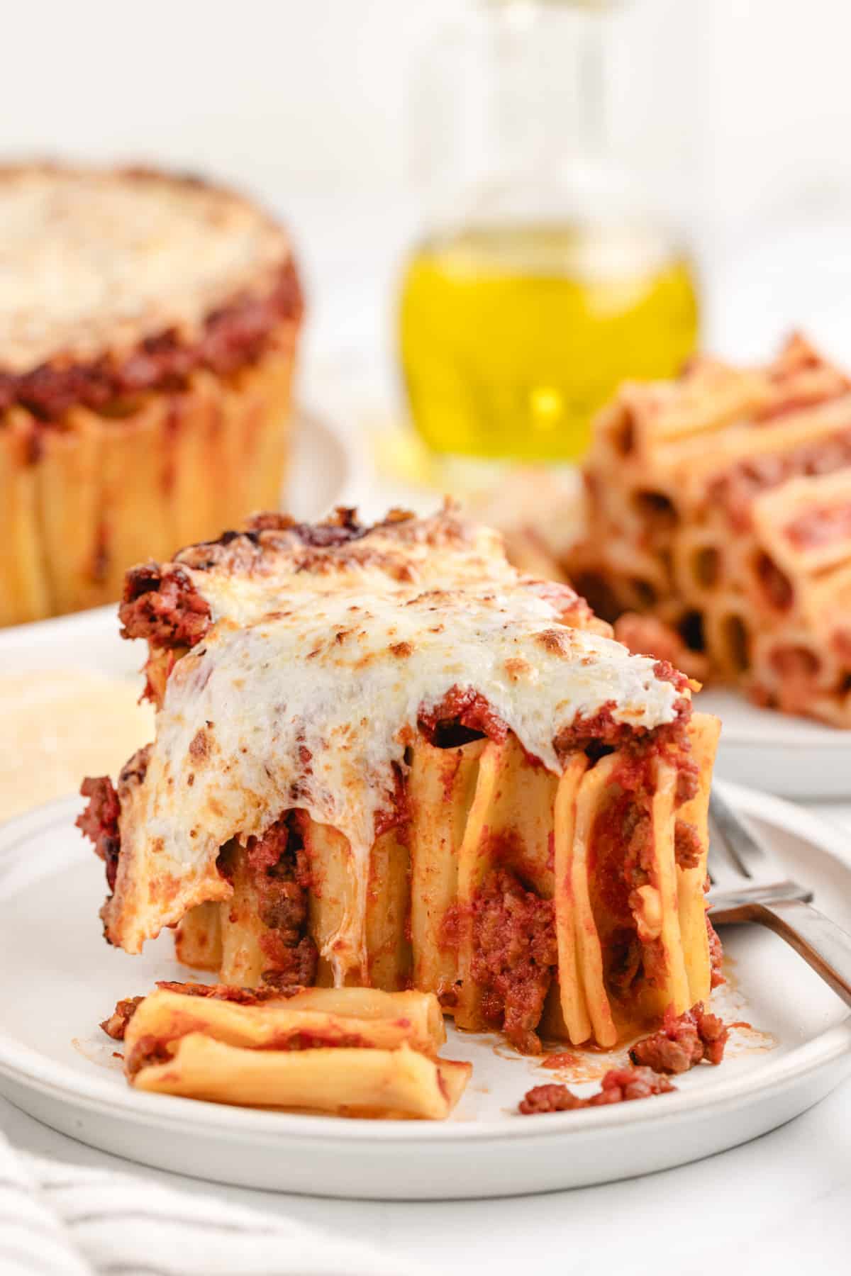 A piece of pasta pie A single slice of pasta pie on a plate, with gooey melted mozzarella stretching as it's lifted, showing the structured layers of pasta and sauce.