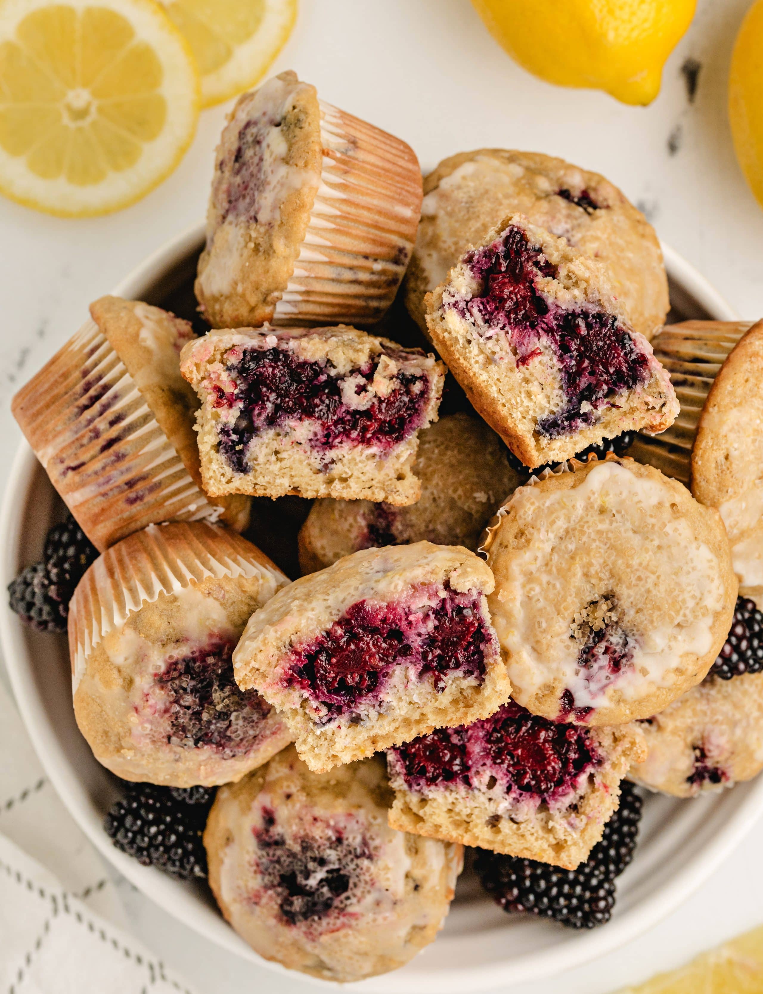 halved lemon blackberry muffins with oats in a white bowl surrounded by fresh fruit