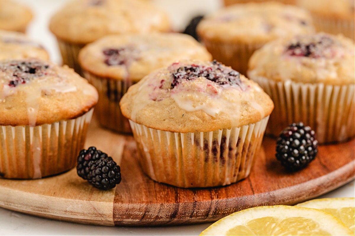 bakery-style lemon blackberry muffins topped with coarse sugar and glaze on a wooden board