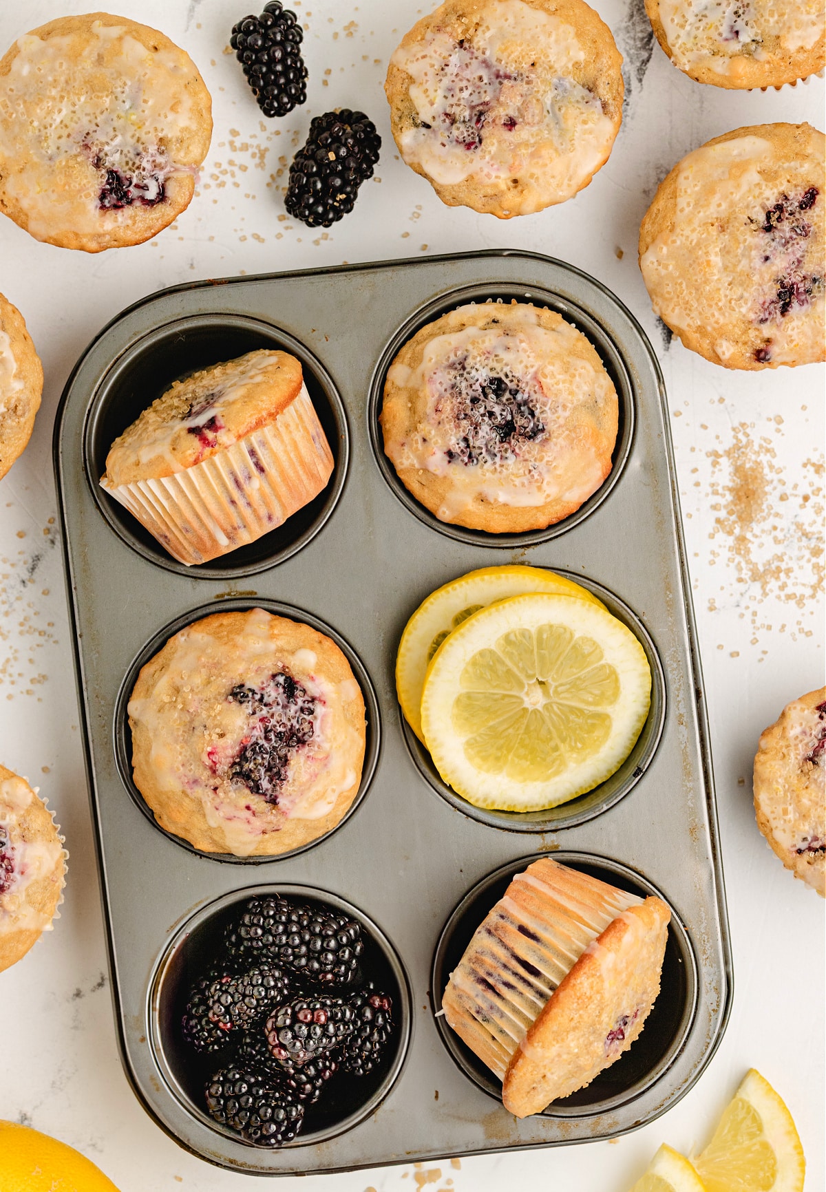 muffin tin filled with baked lemon blackberry muffins, fresh berries, and lemon slices for garnish 