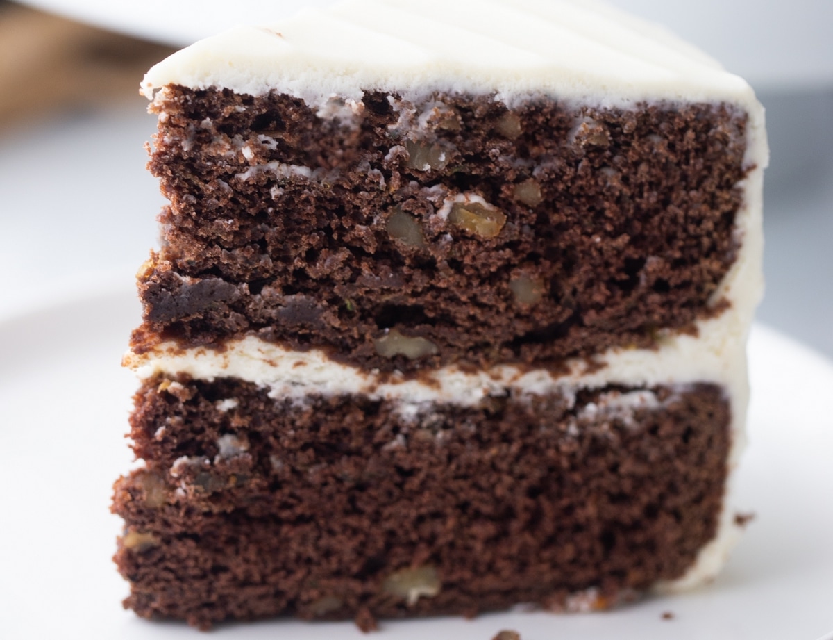 Close-up of moist chocolate zucchini cake layers with visible chopped walnuts and cream cheese frosting.