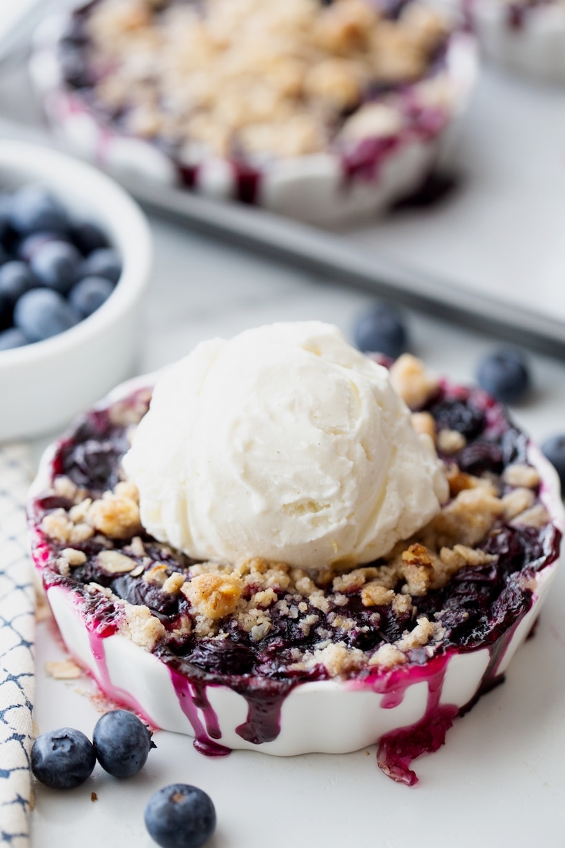 blueberry crisp with ice cream on baking sheet Baked blueberry crisp in ramekin with melting vanilla ice cream on top, resting on baking sheet