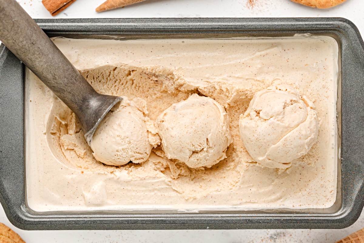 Three scoops of cinnamon ice cream in a loaf pan with a metal scoop.