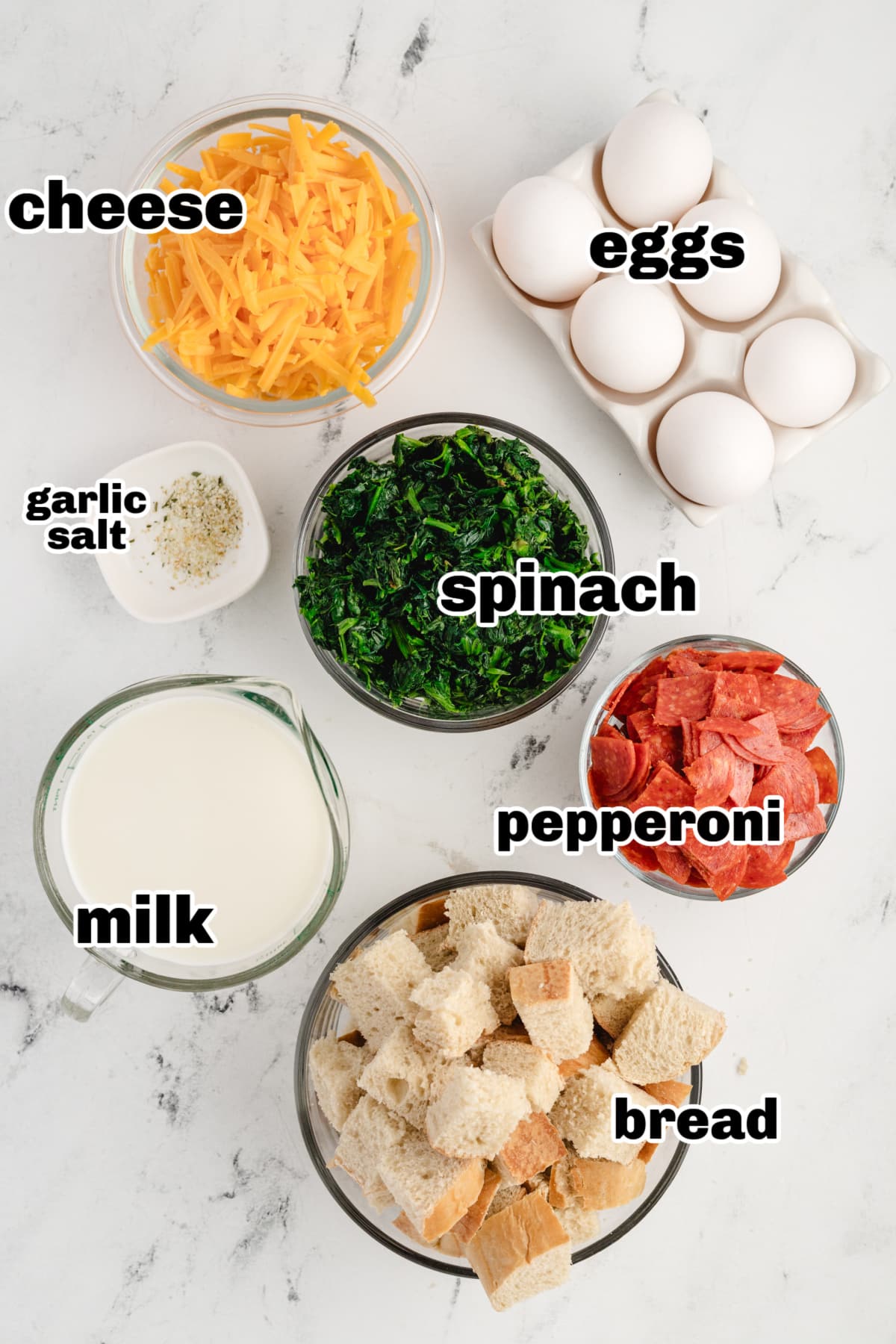 Cheesy Pepperoni Strata ingredients Overhead view of ingredients for cheesy pepperoni strata including bread, eggs, milk, pepperoni, spinach, and cheddar cheese.