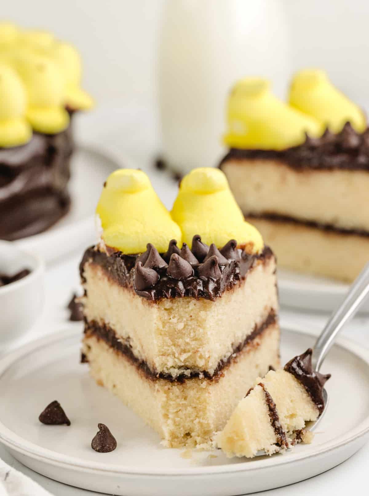 Close-up front view of a slice of Peeps Sunflower Layer Cake with a bite missing, showing the soft yellow cake and thick chocolate frosting.