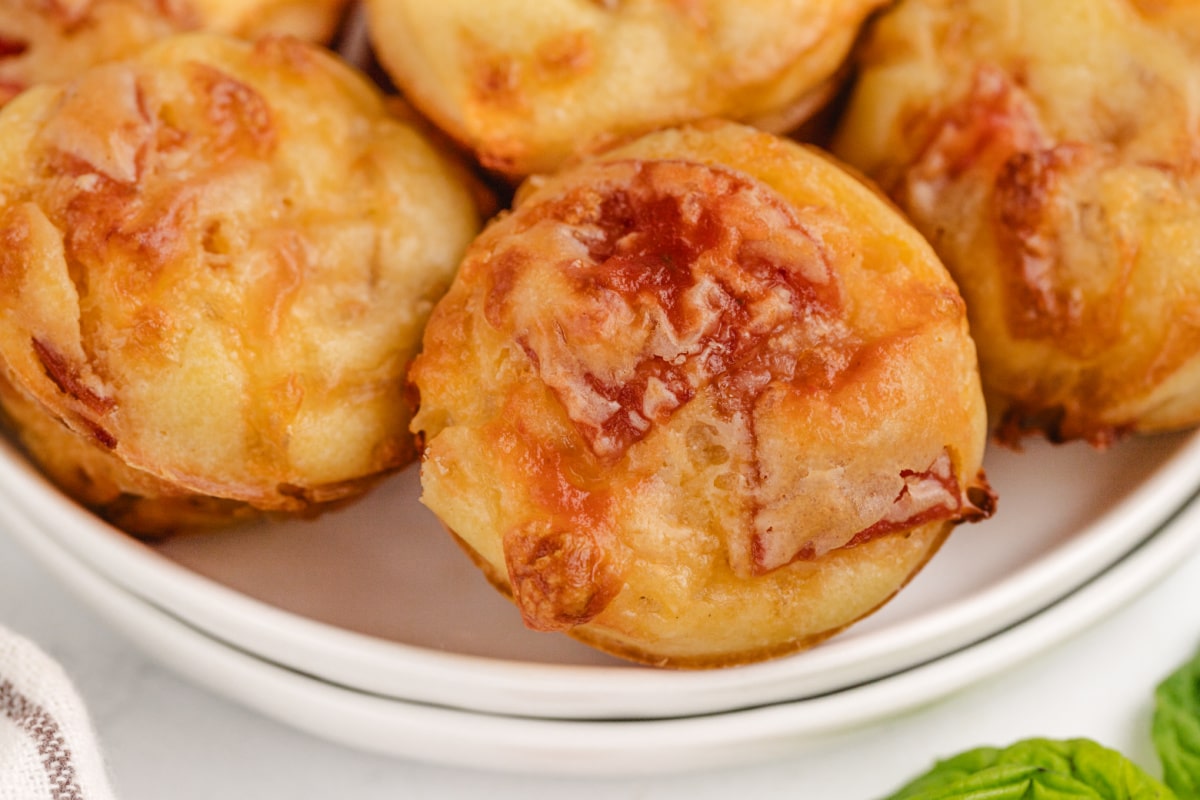 A plate filled with golden brown pepperoni pizza puffs, showing their soft, fluffy centers and crispy exterior.