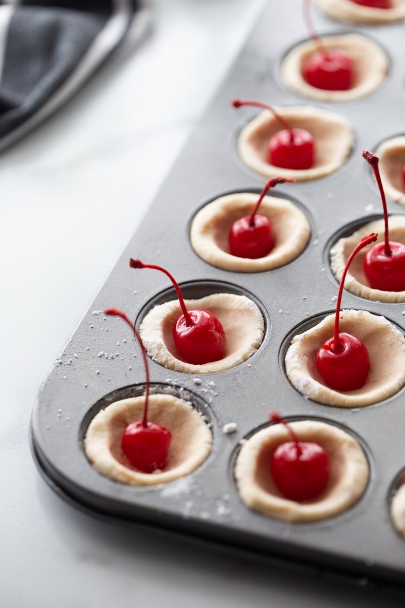 Long stemmed maraschino cherries burst right out the top of these pillowy-soft and bite-sized pastry pouch cookies. They are the perfect addition to any dessert table. how to make tassies