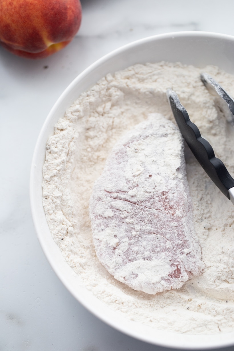 Dredging pork chops in flour before pan searing Boneless pork chop being dredged in seasoned flour