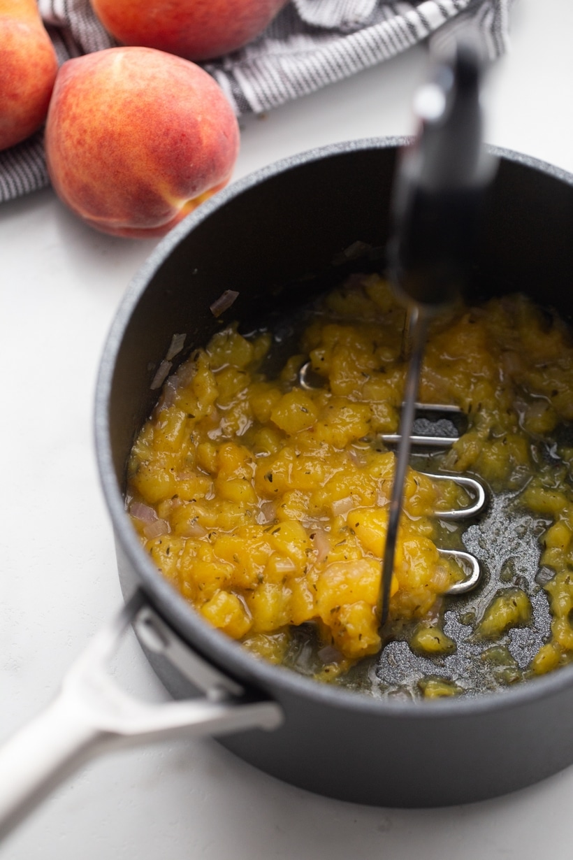 Mashing the cooked chutney until chunky Peach chutney being mashed in the saucepan after simmering