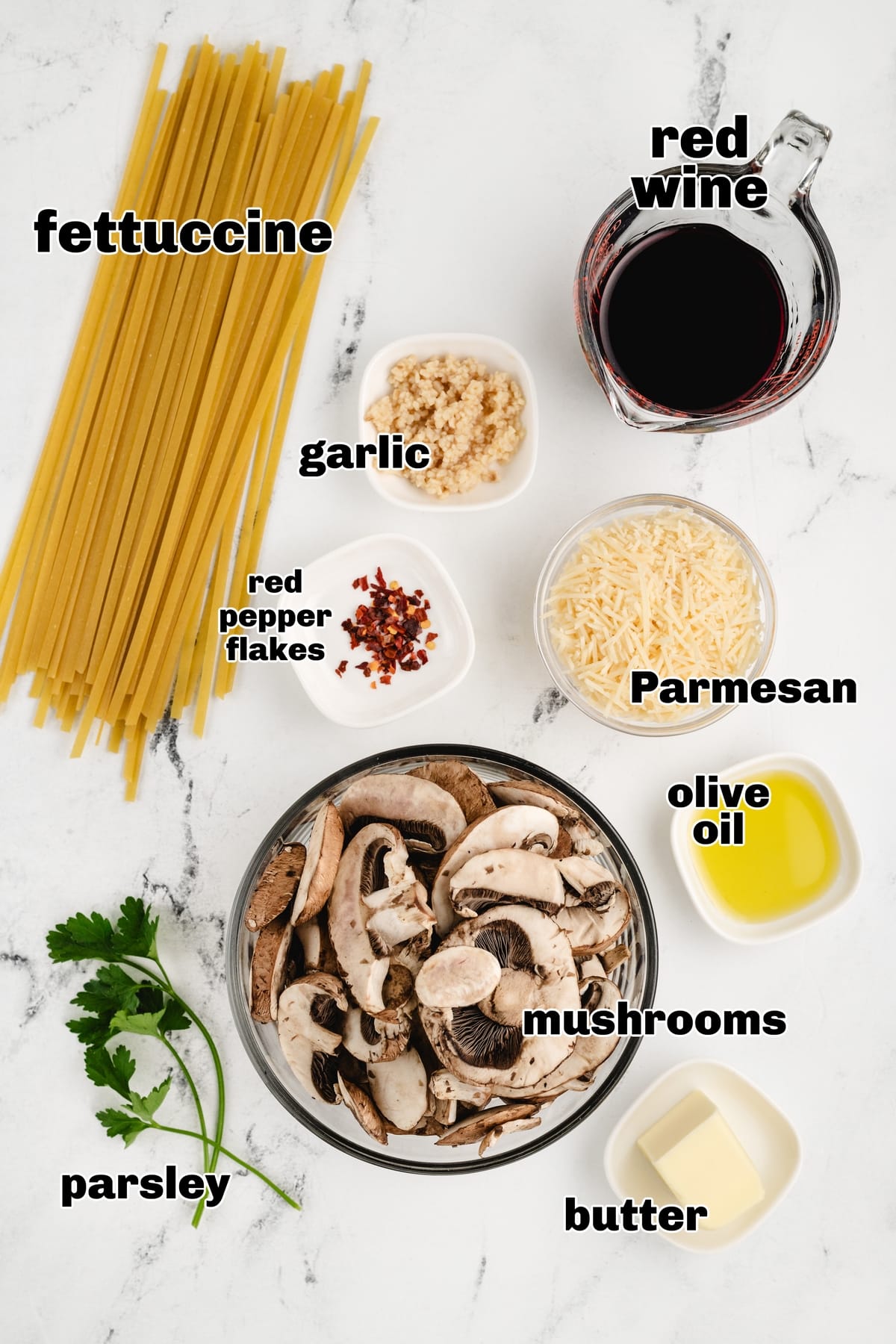 Ingredients laid out for creamy mushroom fettuccine including pasta, mushrooms, garlic, Parmesan, red wine, and parsley