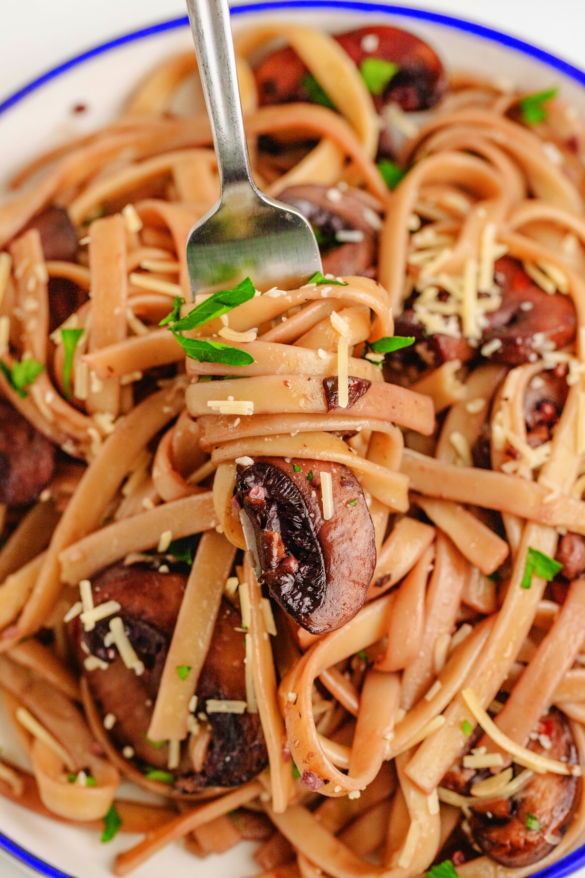 Creamy mushroom fettuccine twirled on a fork with sautéed mushrooms and parsley