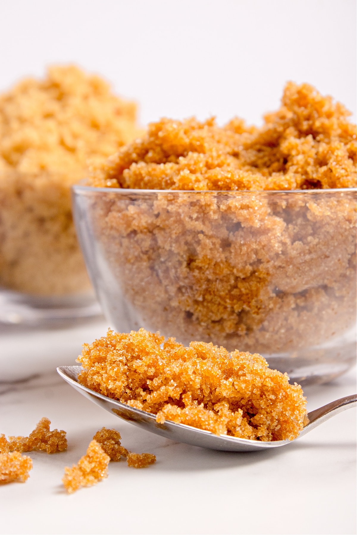 Light brown sugar mounded in a glass bowl. A close-up view of light brown sugar in a glass bowl, with a second bowl of brown sugar softly blurred in the background.
