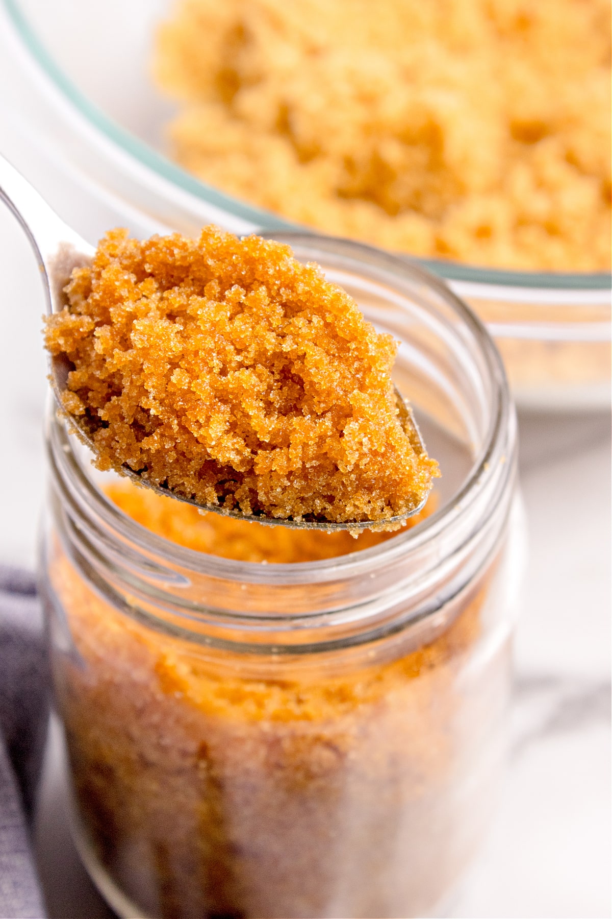 A spoonful of homemade brown sugar taken from a glass jar. A spoonful of homemade brown sugar being lifted from a glass jar, showing the soft, moist texture and rich molasses color.