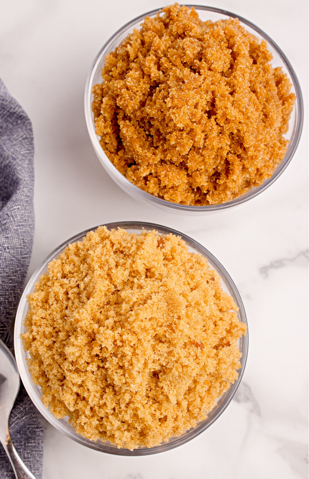 Light and dark brown sugar side by side in glass bowls. Two glass bowls filled with light and dark homemade brown sugar, showing the difference in color and the soft, crumbly texture of each.