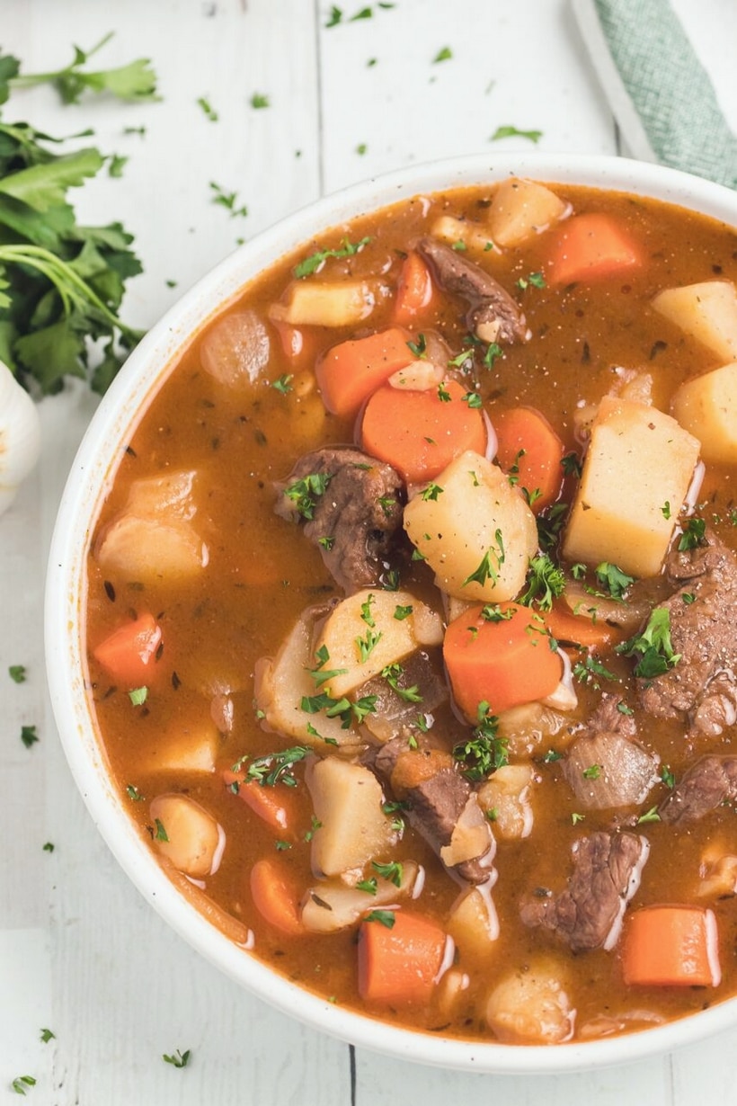 Beef Irish Stew overhead Overhead shot of Beef Irish Stew served in a rustic bowl with a spoon, with a loaf of crusty bread in the background.
