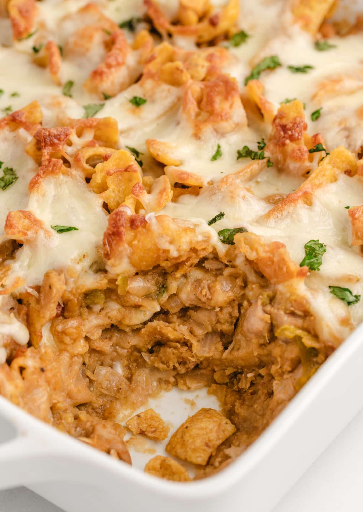 Chicken Frito Pie Casserole with a scoop removed, showing layers of chicken, beans, melted cheese, and Fritos.